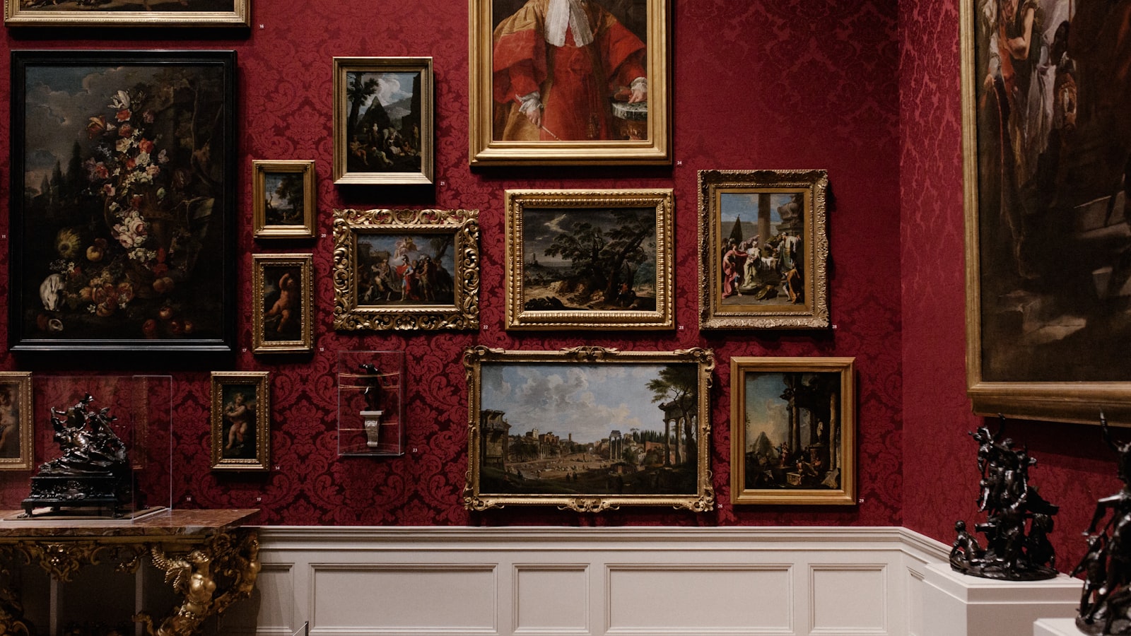 Galeria de museu com obras emolduradas em parede vermelha e esculturas